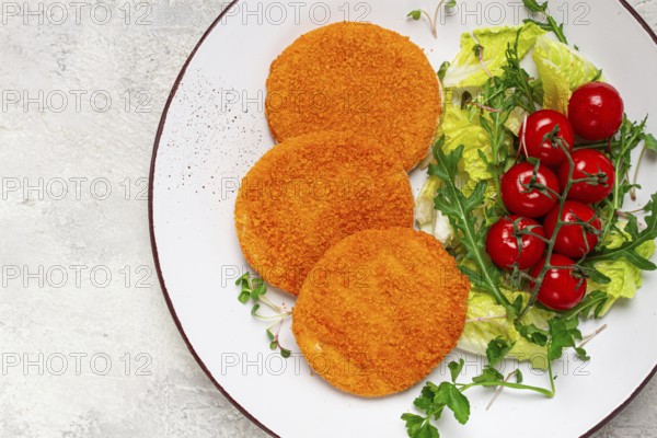 Crispy fried fish cutlets, fish burgers, on a white plate, with fresh lettuce leaves, arugula and cherry tomatoes, homemade, no people