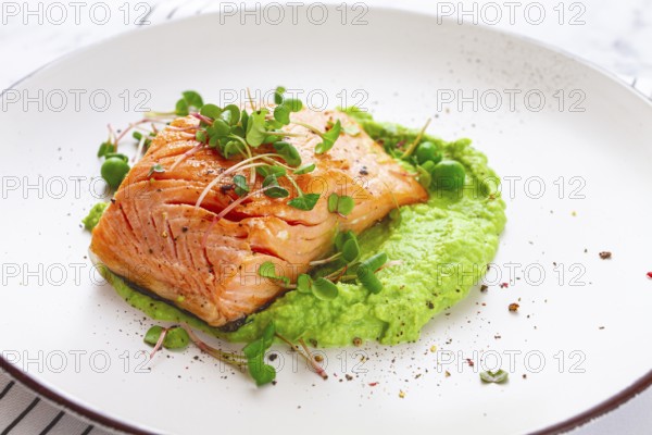 Delicious grilled salmon is placed elegantly on creamy green pea puree. Fresh microgreens and peas add a bright touch, creating an appetizing dish perfect for any meal