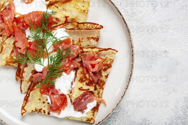 Delicious pancakes with salmon and sour cream, breakfast, on a plate, rustic style, with cutlery