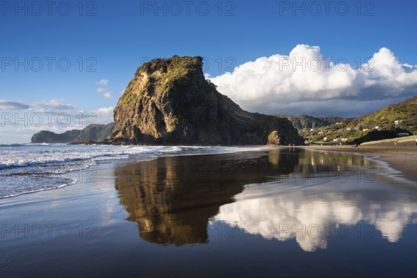 Landscape in New Zealand with sea and sandy beach. Piha Beach and Lion Rock. People on the beach, surfers in the water. Piha, Waitakere Ranges, West Auckland, New Zealand