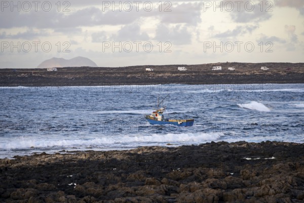 Fishing boat out to sea in the evening, seaside coast with volcanic rocks at sunset, La Santa, Lanzarote, Canary Islands, Spain
