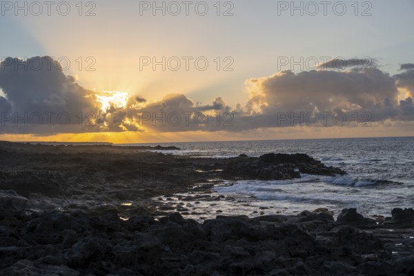 Dramatic cloudy sky with sunbeams at sunset, seaside coast with volcanic rocks, La Santa, Lanzarote, Canary Islands, Spain