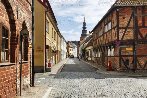 Charming cobblestone street, traditional half-timbered houses and brick buildings, St. Mary's Church tower, stroller, old town of Ystad, Sweden