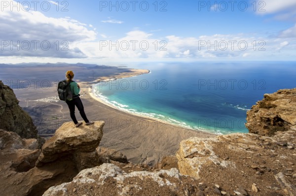 Young woman enjoying the view from the Risco de Famara cliffs to Famara beach, Playa de Famara with La Calaeta, Lanzarote, Canary Islands, Spain