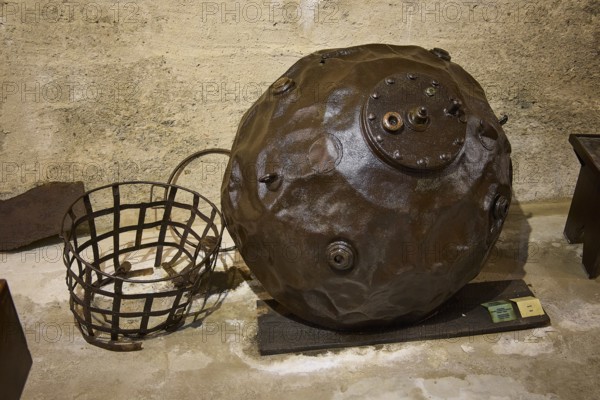 An ancient sea mine next to a metal basket on a concrete floor, War Museum, Military Museum, Tunnel Museum, Lakki, Leros, WW2, Dodecanese, Greek Islands, Greece