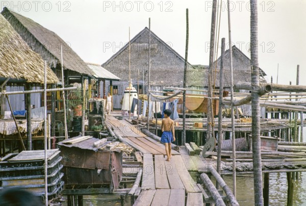 Wooden plank walkway past attap houses of fishing village on stilts, Singapore, southeast Asia 1963