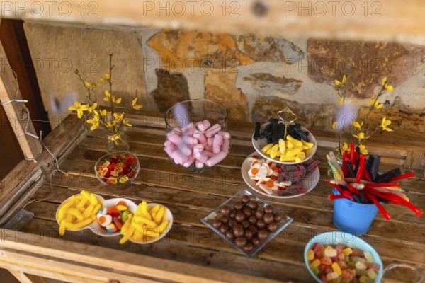 Delicious assortment of colorful candies presented on wooden table at a wedding reception, creating a vibrant and tempting candy bar