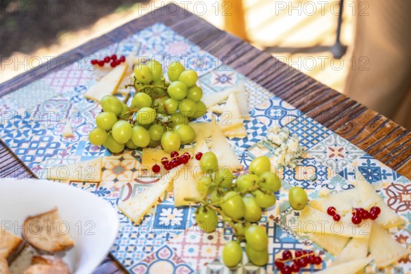 Slices of cheese, bunches of green grapes, and red currants are beautifully arranged on a vibrant tablecloth, creating an enticing appetizer platter for a wedding celebration