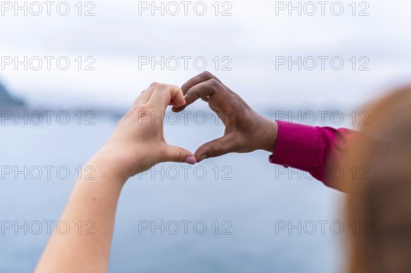 Bride and groom forming a heart shape with their hands against a stunning seascape, celebrating love and unity on their wedding day