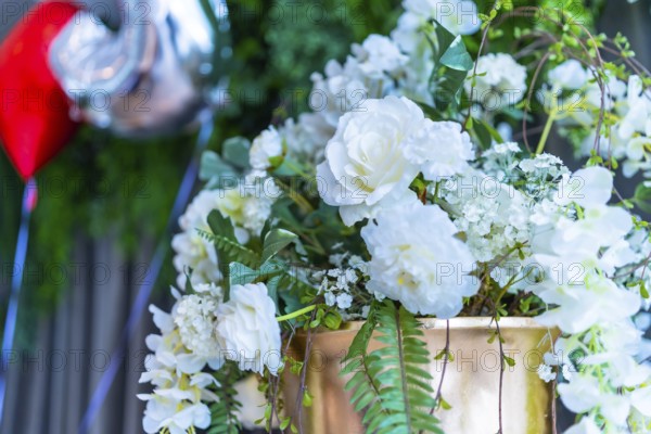 Elegant white roses and greenery adorn a golden vase, adding a touch of romance to a wedding celebration with balloons floating in the background