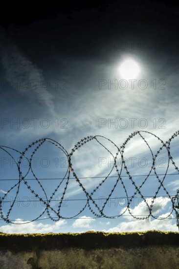 Barbed wire fence under a bright sun against a clear blue sky during the day