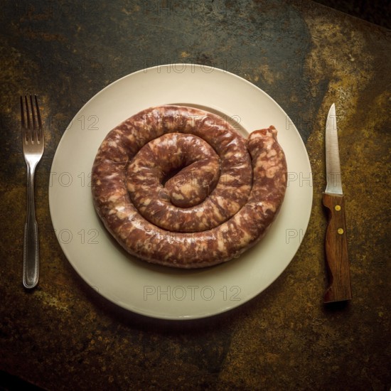 Pork sausage on a white plate surrounded by a knife and fork at a rustic table