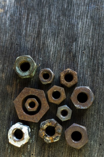Collection of rusted metal nuts arranged on a weathered wooden surface highlighting unique textures and shapes