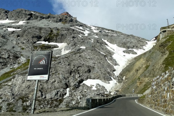 Warning sign against driving too fast too high speed Danger of losing control with stylised speedometer and lettering No Credei on east ramp in front of hairpin bends of Stelvio Stelvio Alpine Pass, top centre on the rock Gasthof Hotel Tibethaus, Stelvio Pass, Stelvio, Autonomous Province of Bolzano, South Tyrol, Italy