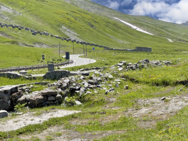 View of the front foundation walls ruins of 2000 year old historical ancient Roman hostel Mansio at the top of the Alpine pass Colle del Piccolo San Bernardo, Col du Petit Saint Bernard Little Saint Bernard Pass in the Alps, behind it modern pass road, in the background on the left on the slope remains of former border fortifications from World War II, Aosta Valley region, Italy