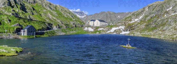 Panoramic photo of mountain lake Alpine lake Lac du Grand Gd Saint St Bernard, on the left Swiss border station border building for passport control, on the right in front Christian cross on small rocks in the lake near the shore centre in the background building with hostel Auberge and Hospice Hospice on Alpine pass Great Saint Bernard Col du Grand Gd Saint St Bernard Colle del Gran San Bernardo, Aosta Valley region, Italy, Canton Valais, Switzerland