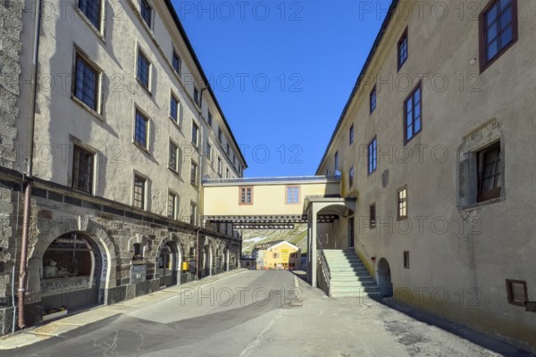 Alpine road with pass summit of Alpine Pass Grenzpass Großer Sankt St. Bernhard Pass leads through between left Auberge right Hospice du Grand Saint Bernard, in the centre bridge with connecting passage between hotel and hospice over pass road, Col du Grand Gd Saint St Bernard Colle del Gran San Bernardo, Canton Valais, Switzerland