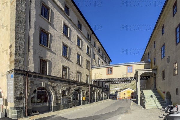 Alpine road with pass summit of Alpine pass border pass Great Saint Bernard Pass leads through between left Swiss Hotel Auberge right Hospice du Grand Saint Bernard, in the centre bridge with connecting corridor between hotel and hospice over pass road, Col du Grand Gd Saint St Bernard Colle del Gran San Bernardo, Canton Valais, Switzerland