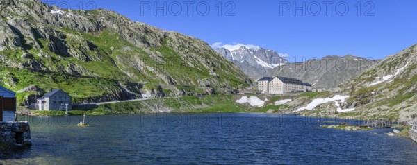 Panoramic photo of mountain lake Alpine lake Lac du Grand Gd Saint St Bernard, on the left Swiss border station border building for passport control, centre in the background building with hostel Auberge and hospice Hospice on Alpine pass Great Saint Bernard Col du Grand Gd Saint St Bernard Colle del Gran San Bernardo, region Valle d'Aosta, Italy, canton Valais, Switzerland