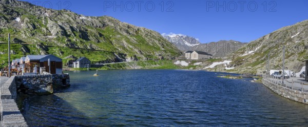 Panoramic photo of mountain lake Alpine lake Lac du Grand Gd Saint St Bernard, on the left souvenir shops, behind it Swiss border station border building for passport control in the background building with hostel Auberge and hospice Hospice on Alpine pass Great St Bernard Col du Grand Gd Saint St Bernard Colle del Gran San Bernardo, region Valle d'Aosta, Italy, canton Valais, Switzerland