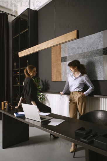 Two women engage in a productive discussion in a sleek office with dark walls and contemporary decor