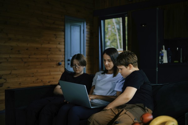 The family enjoys spending time together watching a movie on a laptop in a cozy wooden cabin