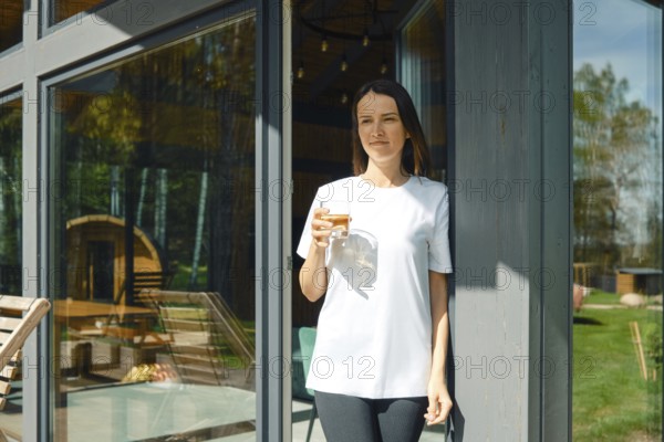 The woman went to the terrace of a country house with a glass of juice and enjoys silence and fresh air. The concept of life in nature away from the city