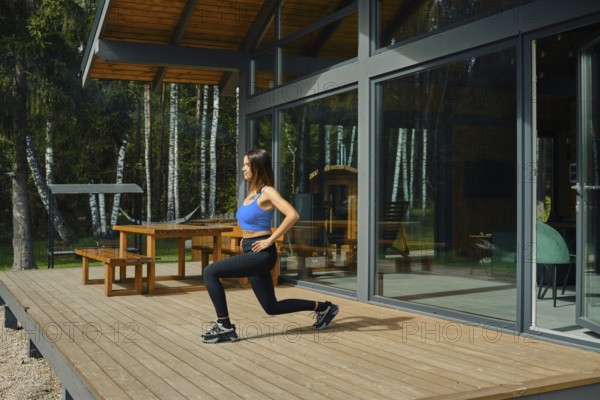 A woman in athletic wear practices lunges on a spacious wooden deck of a modern cabin. Surrounded by trees, the setting is peaceful and suggests an outdoor workout
