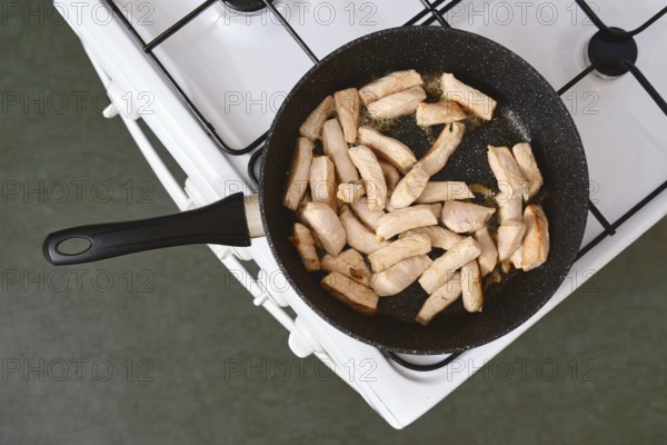 Sizzling pieces of pork fillet cooking in a frying pan on a gas stove in a kitchen setting