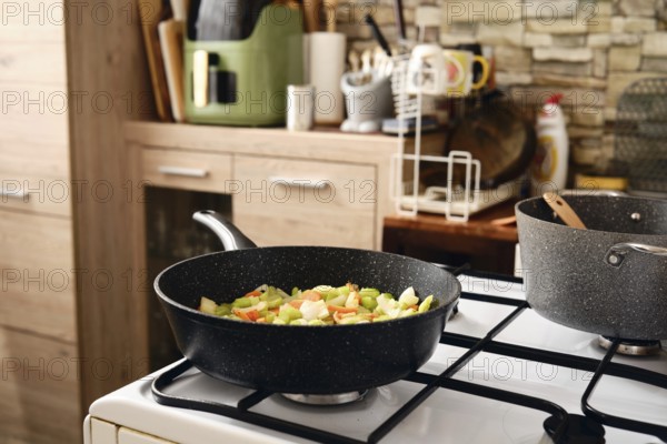 Fresh vegetables in a frying pan on the stove, showcasing a vibrant mix of colors. A cozy kitchen with wooden cabinets and modern appliances enhances the cooking experience