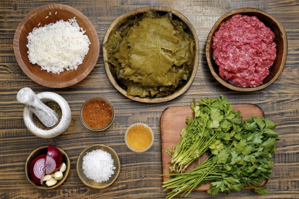 Ingredients to make dolma at home. Grape leaves, minced meat, rice, and various spices and herbs are arranged on a wooden kitchen table
