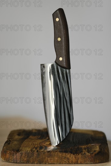 Serbian kitchen knife stuck in a rustic wooden block. The knife features a sleek, shiny blade with unique patterns and a dark wooden handle. Ideal for culinary enthusiasts
