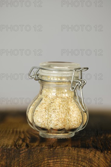 Glass jar filled with garlic flakes on a wooden surface against a neutral background