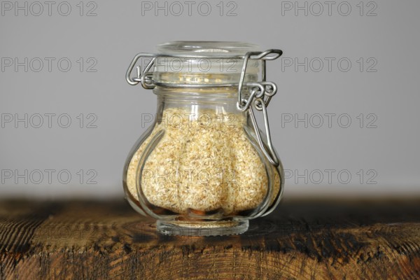 A small, decorative glass jar with garlic flakes, showcasing its fine texture and color on a rustic wooden surface