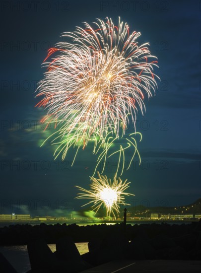 Brilliantly shining, atmospheric, intense fireworks in red, green and gold, Heligoland island festival, nocturnal lowlands, inland harbour, jetty and lobster shacks, midland, in front the tetrapod dune platforms and the reflecting waters of the North Sea, Night sky at the island festival in summer, symbolic image also for New Year's Eve, New Year's Eve fireworks, bright, colourful, many colourful traces of light, sparks, lively glitter, night, Heligoland Island, Schleswig-Holstein, Germany