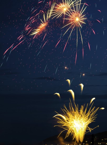 A brilliantly radiant, atmospheric firework display for the Heligoland island festival in red and gold over the nightly lowlands with a golden fire fountain and three swirling stars, night sky at the island festival in summer, symbolic image also for New Year's Eve, New Year's Eve fireworks, bright, colourful, brilliant, many colourful traces of light, sparks, lively glitter, night, Heligoland island, Schleswig-Holstein, Germany