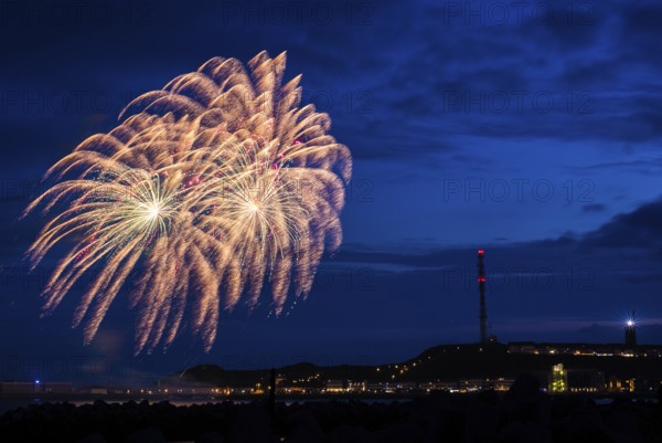A brilliantly shining, atmospheric firework display for the Heligoland island festival in red and gold, Unterland with inland harbour, jetty and lobster shacks, on the right the Oberland with transmission tower, transmitter and lighthouse at night, in front the groynes of the dune, reflecting water of the North Sea, night sky at the island festival, summer, symbolic image also for New Year's Eve, New Year's Eve fireworks, bright, colourful, many colourful traces of light, lively glitter, night, Heligoland Island, Schleswig-Holstein, Germany