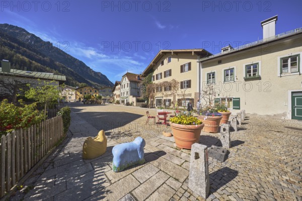Old town, historic houses, square, cobblestones, bollards, wooden fence, facade, windows, bushes, flower pots, Easter decoration, mountain landscape, mountains, forest, blue sky, cirrostratus clouds, Florianiplatz, Bad Reichenhall, district Berchtesgadener Land, Bavaria, Germany