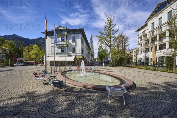 Wisbacherbrunnen, fountain, pedestrian zone, general architecture, cobblestones, flagpoles, flags, trees, blue sky, cirrostratus clouds, crossing of Salzburger Straße with Wisbacher Straße and Ludwigstraße, Bad Reichenhall, district Berchtesgadener Land, Bavaria, Germany