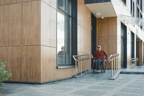 A person in a wheelchair navigates the accessible entrance of a contemporary building, showcasing wheelchair ramps and large windows. The setting is well-lit, indicating a bright day