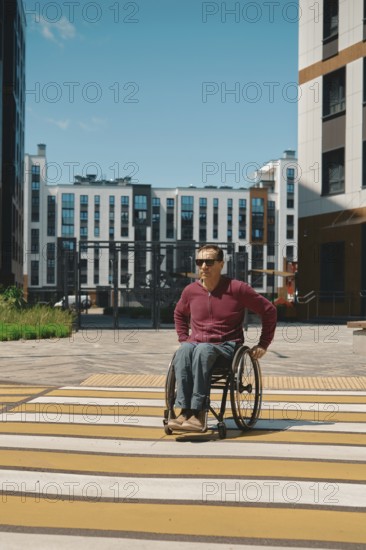A person using a wheelchair navigates a brightly painted crosswalk in a modern urban area. Surrounding buildings and clear blue sky emphasize the vibrant atmosphere of the day