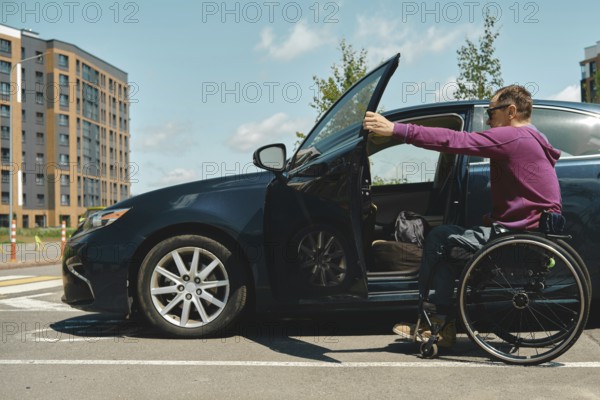 A man in a wheelchair approaches a car parked in a bright urban setting. He is wearing a purple sweater and has a focused expression as he opens the car door