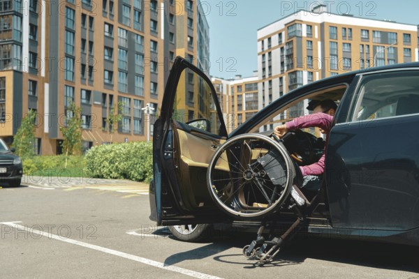 A person is carefully getting out a vehicle using a wheelchair in a bustling parking lot. The background features modern apartment buildings and lush greenery under clear blue skies