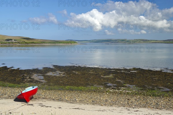 Red boat on the beach with a distant view of the calm sea and a cloudy summer landscape, Hoy, Orkney Islands, Scotland, United Kingdom