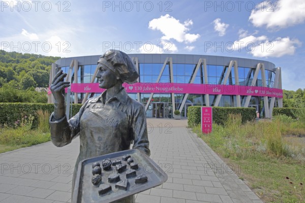 Sculpture confectioner with tray full of pralines for tasting, presentation, eating, enjoyment, pleasure, look, marvel, look at, enjoy, modern, round, building, glass window, pink banner with inscription, anniversary 130 years of nougat love, chocolate factory, sale, production and manufacture of sweets, chocolate, nougat, confectionery, confectioner, chocolate, food, Viba Nougat World, Schmalkalden, Franconia, Thuringia, Germany