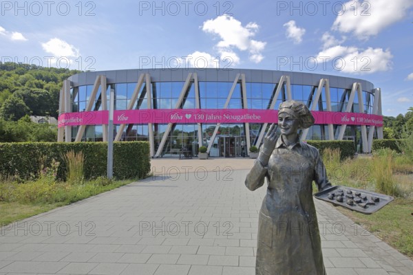 Sculpture confectioner with tray of pralines for tasting, modern, round, building, glass window, pink banner with inscription, anniversary 130 years of nougat love, confectionery, chocolate factory, sale, production and manufacture of sweets, food, chocolate, Viba Nougat World, Schmalkalden, Franconia, Thuringia, Germany