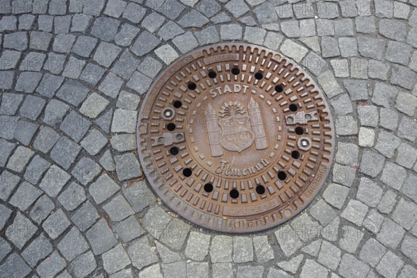 Round manhole cover with town coat of arms, inscription, cobblestones, floor, Ilmenau, Thuringian Forest, Thuringia, Germany