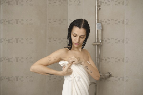 In a modern bathroom, a woman with damp hair adjusts her towel after taking a shower. She appears relaxed as she prepares for her morning routine in a bright and inviting space