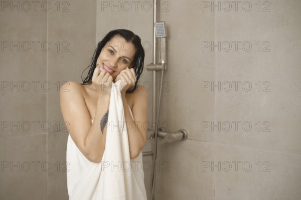 A woman stands in a modern bathroom, smiling while holding a towel close to her body. The warm light accentuates the minimalist design, giving a serene and inviting atmosphere