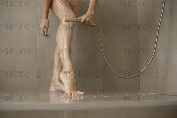 Water cascades over female legs in a sleek bathroom. The individual uses a handheld showerhead to clean and refresh while standing on a tiled floor
